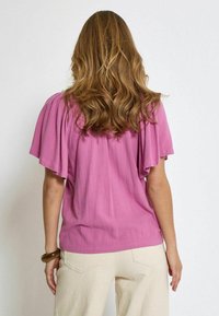 Corta blusa rosa con maniche a sbuffo, realizzata in materiale leggero. Abbinala a pantaloni larghi crema, con tasche e una vestibilità morbida.
