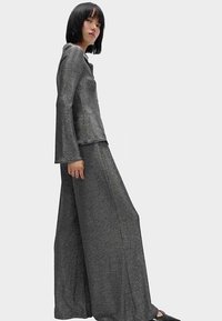 Haut métallisé gris à manches longues évasées, assorti à un pantalon large. Texture lisse et design minimaliste sans motifs.