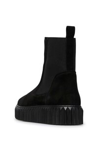 Stivaletti neri alla caviglia con una tomaia in suede liscia, pannelli laterali elastici e una suola piatta nera testurizzata con un design rigato.