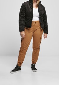 Brązowe spodnie cargo z elastycznymi mankietami, połączone z czarną kurtką pikowaną z korduroju i białym topem, uzupełnione czarnymi sneakersami.