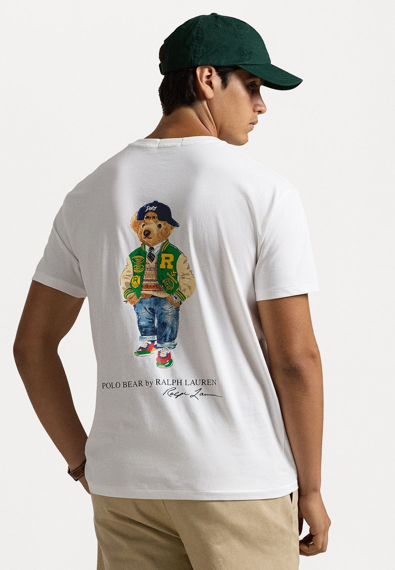 White cotton t-shirt featuring a colorful graphic of a bear in a green varsity jacket, blue jeans, and sneakers, with "Polo Bear" text below.
