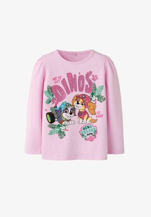 Różowa koszulka z długim rękawem z dwoma animowanymi psami noszącymi kaski, otoczona liśćmi, z tekstem "We've got dinos to save" i "Dino Island."
