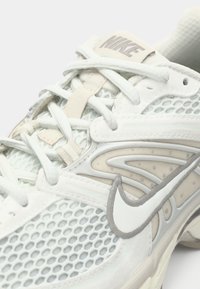 Białe i beżowe buty biegowe Nike z siateczkowym wierzchem, grubymi sznurowadłami i wyraźnym logo Nike na boku.