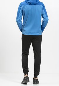 Modrá bunda s kapucí a kontrastními rukávy, doplněná černými tepláky. Má elastické manžety a pohodlnou černou obuv.