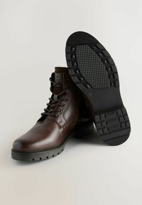 Bruine leren veterschoenen met een gladde textuur, een gewatteerde kraag en een robuuste zwarte rubberen zool met een patroon in het profiel.