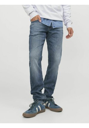 Jean en denim bleu foncé à coupe droite, légèrement délavé, design à cinq poches, porté avec une chemise boutonnée bleu clair et des baskets bleues.