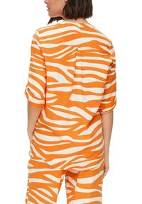 Orangene und weiße gestreifte Bluse mit entspanntem Schnitt, kurzen Ärmeln und einem Faltenelement auf der Rückseite. Hergestellt aus leichtem Stoff.