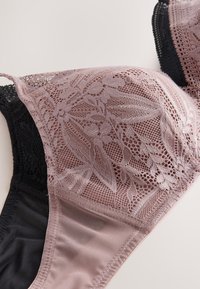 Spitzen-BH mit Blumenmuster in Mauve und Schwarz, mit transparentem Mesh-Material und strukturierter Körbchengestaltung auf hellem Hintergrund.