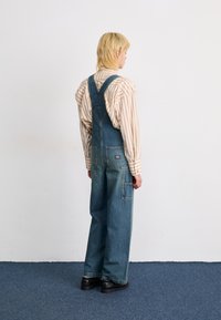 Denimbyxor i ljusblått med vida ben, justerbara axelband och två framfickor. Matchat med en randig långärmad skjorta.