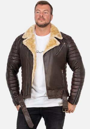 Veste en cuir marron avec un col en fourrure, des manches côtelées, des zippers sur les poches et un détail de ceinture à la taille. Fini texturé sur l'ensemble.