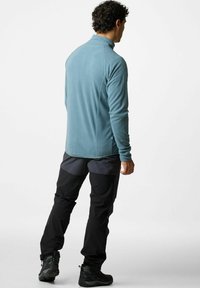 Giacca in pile azzurro chiaro con colletto alto, abbinata a pantaloni tecnici neri con tasche con cerniera e ginocchia rinforzate. Tessuto testurizzato.