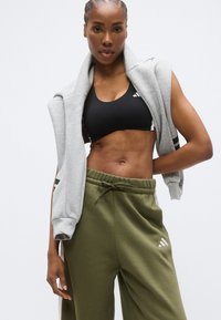 Czarny sportowy biustonosz z białymi akcentami, szara bluza narzucona na ramiona, oliwkowo-zielone spodnie dresowe o luźnym kroju, casualowy strój sportowy.