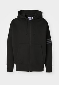 Svart zip-up hoodie i mjukt material. Har en känguruficka, dragsko i huvan och ett design med tre ränder på ena ärmen. Litet logotyp vid fållen.