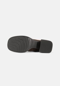 Brown suede shoe with a textured black rubber sole. Features a tapered heel and wavy tread pattern for traction.