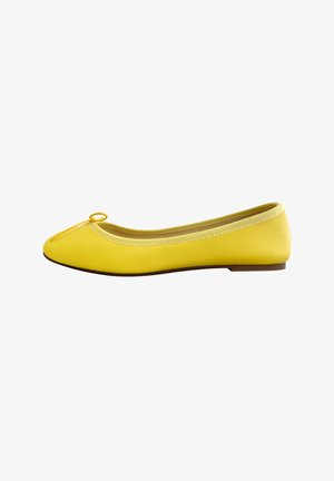Ballerine jaune avec un bout rond, en matériau synthétique lisse, un petit nœud décoratif sur le bout et une semelle basse marron.