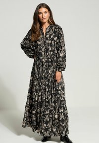 Mustapahka maxi-mekko, jossa on paisley-kuvio, pitkät hihat, napitettava etuosa ja kerroksellinen hameosa. Pehmeä kangas, jossa on väljä istuvuus ja hienovarainen tekstuuri.