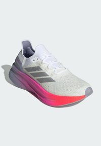 Bílé sportovní boty s texturovaným svrškem, vybavené třemi šedými pruhy, růžovým přechodovým mezipodešví a zaobleným designem špičky.