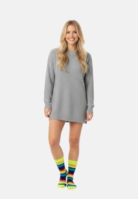 Graues, gestricktes Sweatkleid mit langen Ärmeln, kombiniert mit mehrfarbigen gestreiften Socken in Rot, Blau, Gelb und Grün.