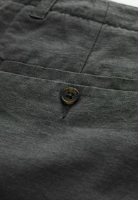 Tissu gris foncé avec une finition texturée, doté d'une fermeture à bouton et d'une poche latérale visible. Le bouton possède une surface lisse et brillante.