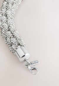 Braided silver bracelet with sparkling clear rhinestones, featuring a chrome clasp and a lobster claw closure. Textured surface and shiny finish.