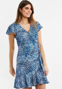 Vestido envolvente de estampado azul y blanco con mangas cortas con volantes, que presenta un escote en forma de V y un dobladillo acampanado, hecho de tela ligera.