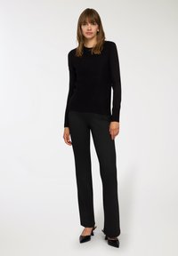 Maglione nero, aderente, realizzato in tessuto morbido, abbinato a pantaloni a vita alta con righe verticali. I pantaloni hanno un leggero svaso e décolleté neri open-toe.