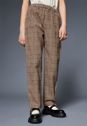 Brown plaid trousers with an elastic waistband, featuring red lines and a relaxed fit. Black platform shoes complete the outfit.