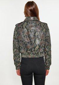 Jachetă scurtă cu model de șarpe, având tonuri de verde, maro și negru. Fabricată dintr-un material texturat, cu talie ajustată și epoleți la umeri.