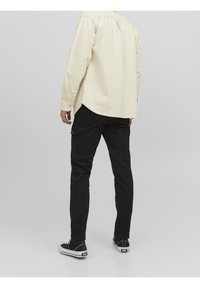 Svarta cargo-byxor med flera fickor, tillsammans med en ljusbeige långärmad skjorta. Outfitten fulländas med svarta sneakers.