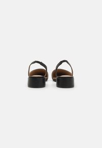 Sandalias abiertas negras con una tira ancha y un tacón grueso. La suela es plana con una textura suave y un forro interior en tonos marrones.