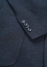 Dark blue textured fabric for a garment, featuring a four-button cuff detail and a notched collar, with visible stitching patterns.