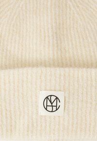 Berretto lavorato a maglia color crema realizzato in morbida lana, con un design a coste testurizzato e un'etichetta rettangolare con logo nero.