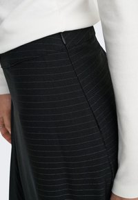 Jupe noire à rayures fines, en tissu lisse, coupe ajustée, avec poches latérales. Conçue avec une fermeture éclair dissimulée et des coutures élégantes.