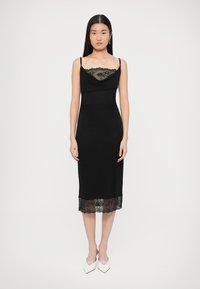 Černé šaty střední délky s volným výstřihem, krajkovou vsadkou na okraji a tenkými ramínky, vyrobené z hladké, přiléhavé látky.