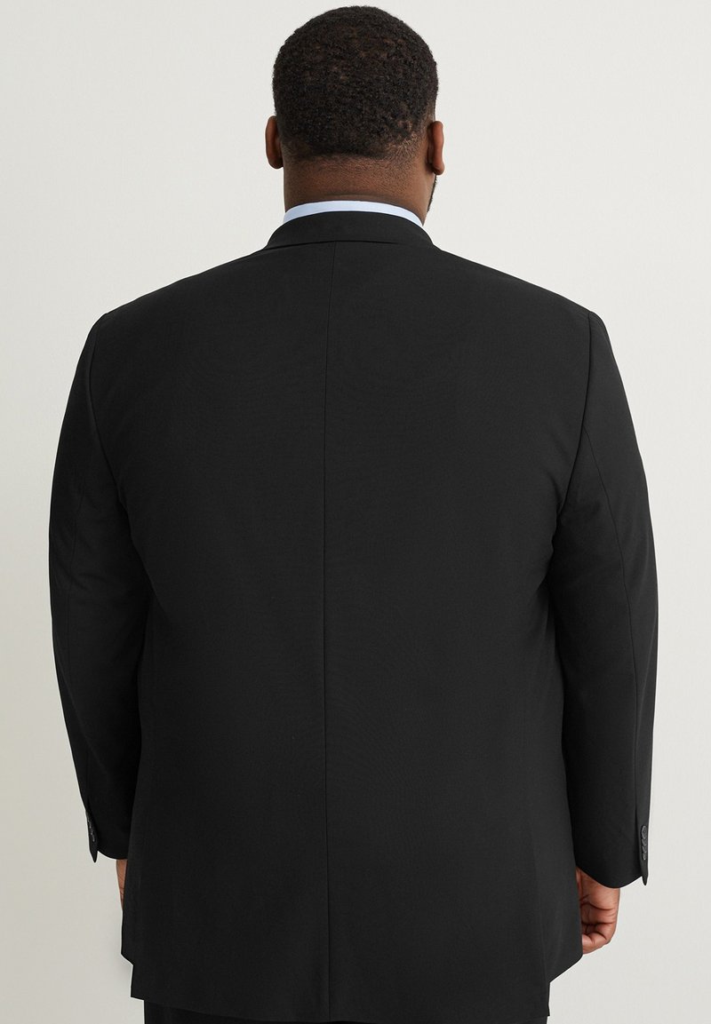 Chaqueta de traje negra con una textura suave y un diseño estructurado, que presenta una costura vertical única, mangas largas y acentos de botones.