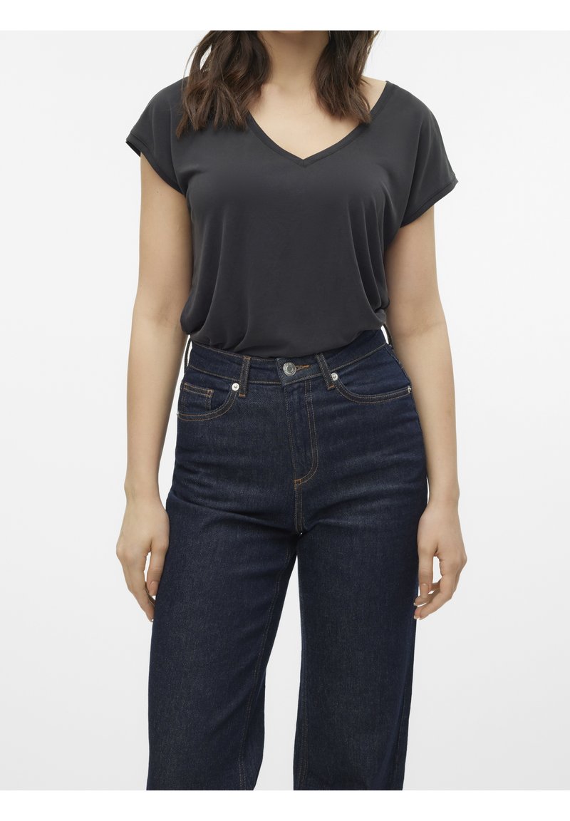 Femme portant un haut noir ample à manches courtes avec col en V, rentré dans un jean droit bleu foncé taille haute.