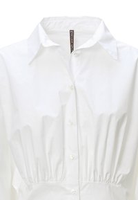 Camicia bianca con colletto strutturato, vita arricciata e texture liscia. Caratterizzata da bottoni trasparenti e un design minimalista.