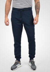 Navy blue joggers made of soft material with a ribbed waistband, adjustable drawstring, and side zippered pockets.
