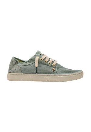 Zapatilla casual de caña baja en tejido verde apagado con cordones beige y una suela de goma beige claro con manchas, exhibida sobre un fondo blanco.