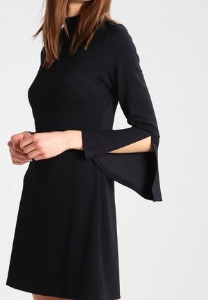 Abito nero con scollatura alta e maniche a tre quarti svasate. Realizzato in un materiale liscio e elasticizzato. Presenta una silhouette aderente e tasche laterali.