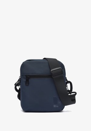 Tamnoplava kvadratna torba na rame s prednjim džepom na patentni zatvarač i podesivim crnim remenom koji se dijagonalno proteže preko torbe.