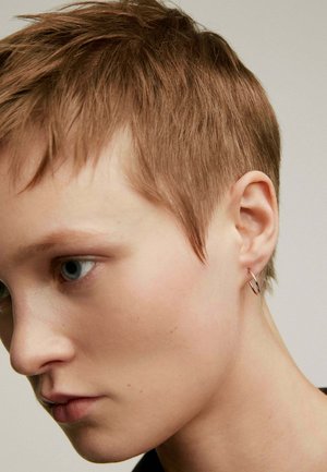 Aro de plata llevado en un cabello corto y texturizado. El primer plano muestra la forma redonda del aro y su acabado de metal liso, resaltando la simplicidad.