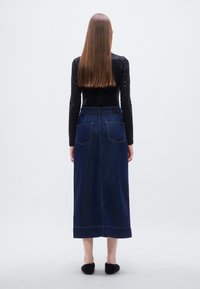 Μακρύ τζιν φούστα σε σκούρο μπλε χρώμα με ψηλό μέση, πίσω τσέπες και διακοσμητικές ραφές σε αντίθετο χρώμα, συνδυασμένη με μαύρο μπλούζα με μακριά μανίκια.