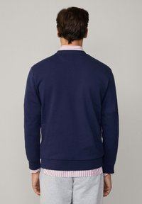 Marineblå crew-neck sweatshirt med ribbet tekstur, tætsiddende manchetter og kant. Laget over en stribet lyserød og hvid skjorte, båret med grå sweats.