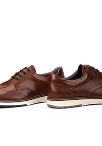 Zapatos de cuero marrón con puntera redondeada, seis ojales y suela blanca en contraste. Textura suave y diseño minimalista con costuras sutiles.