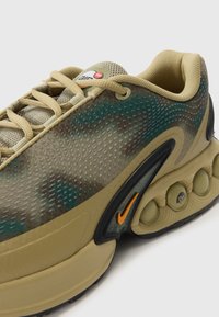 Nike sneakers featuring a camo pattern in green and brown, textured mesh upper, beige accents, and a distinctive air cushioning sole.
