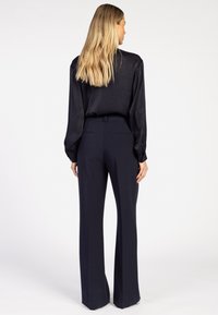 Marineblauwe op maat gemaakte broeken met een wijde poot, gecombineerd met een donkere, gestructureerde blouse met lange mouwen. Gladde stof met een subtiele glans.