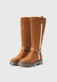 Καφέ σουέτ μπότες μέχρι το γόνατο με γούνα στο εσωτερικό, δερμάτινη ταινία με μεταλλικό κούμπωμα και υφασμάτινη λαβή από καουτσούκ.