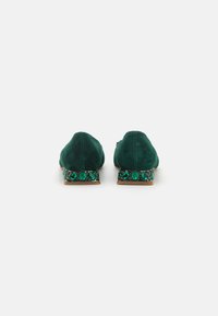 Ballerine verde in suede con tacco basso, decorate con accenti di gemme verdi lucenti sul tacco. Texture liscia nel complesso.