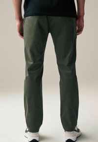Green, lightweight, straight-leg pants with a smooth texture. Features standard pockets and a simple design, paired with white and grey sneakers.